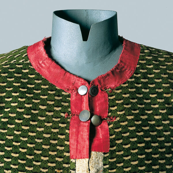 Die Kleiderpuppe trgt ein grn gemustertes Leinen-Miederleibchen aus dem Isarwinkel um 1800. Kragen und Ausschnitt sind in rotem Seidensamt gefertigt, verschlossen von zwei Reihen Metallknpfen.